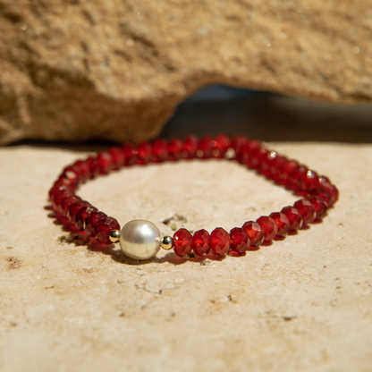 Red beaded bracelet with a pearl on a sandy surface
