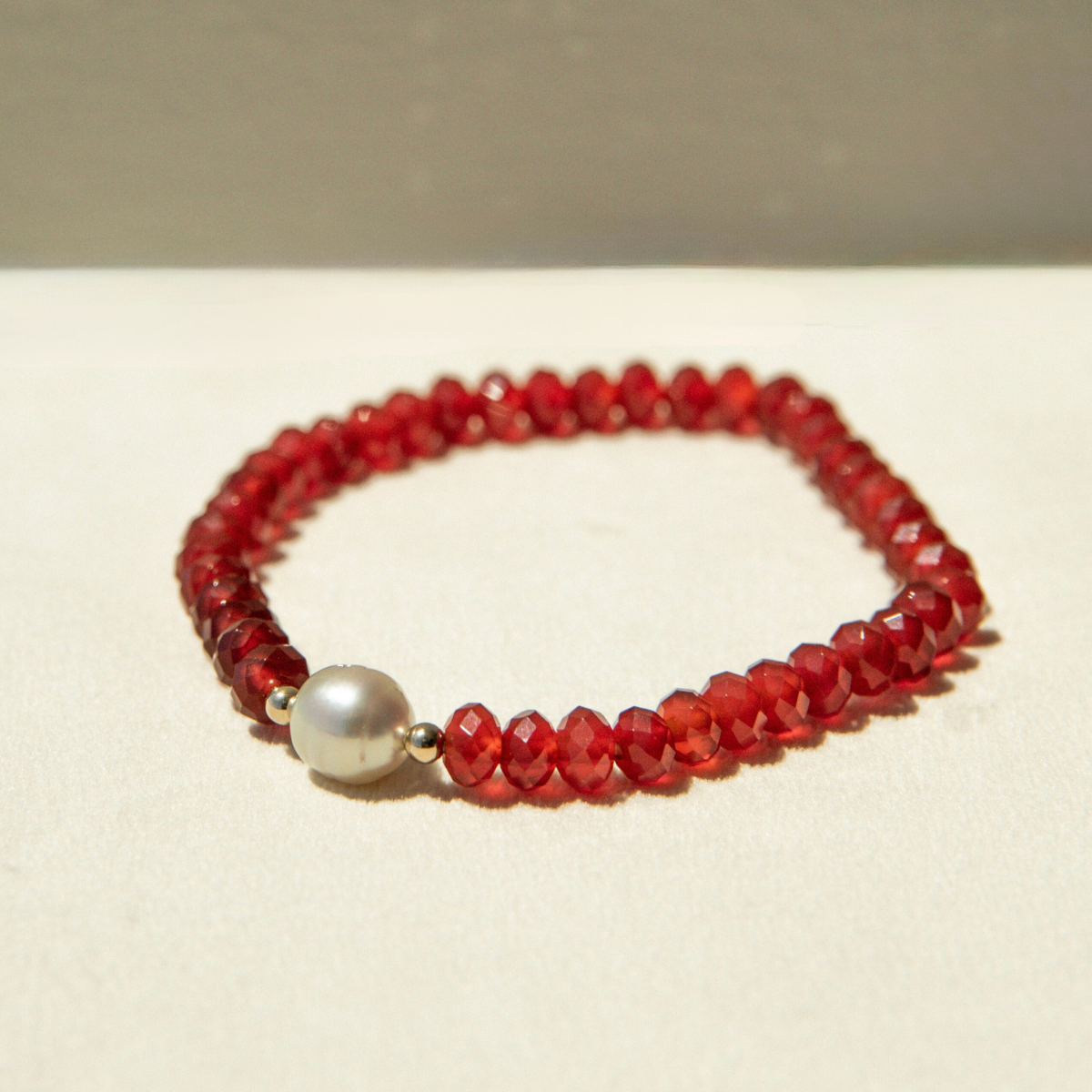 Red beaded bracelet with a pearl on a beige background