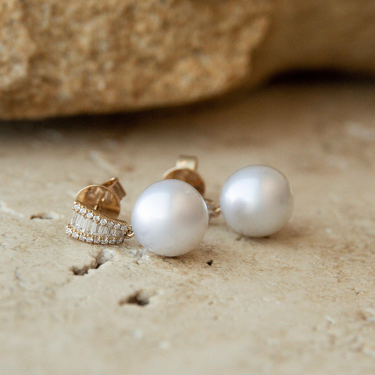 Pearl earrings on a sandy surface with a blurred natural background