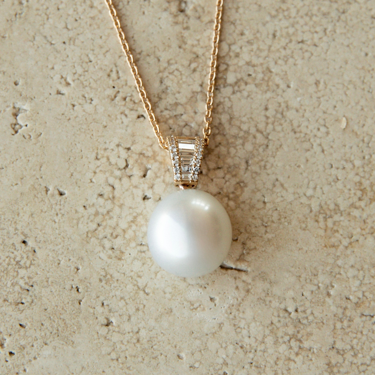 Pearl necklace with gold chain on a beige stone background