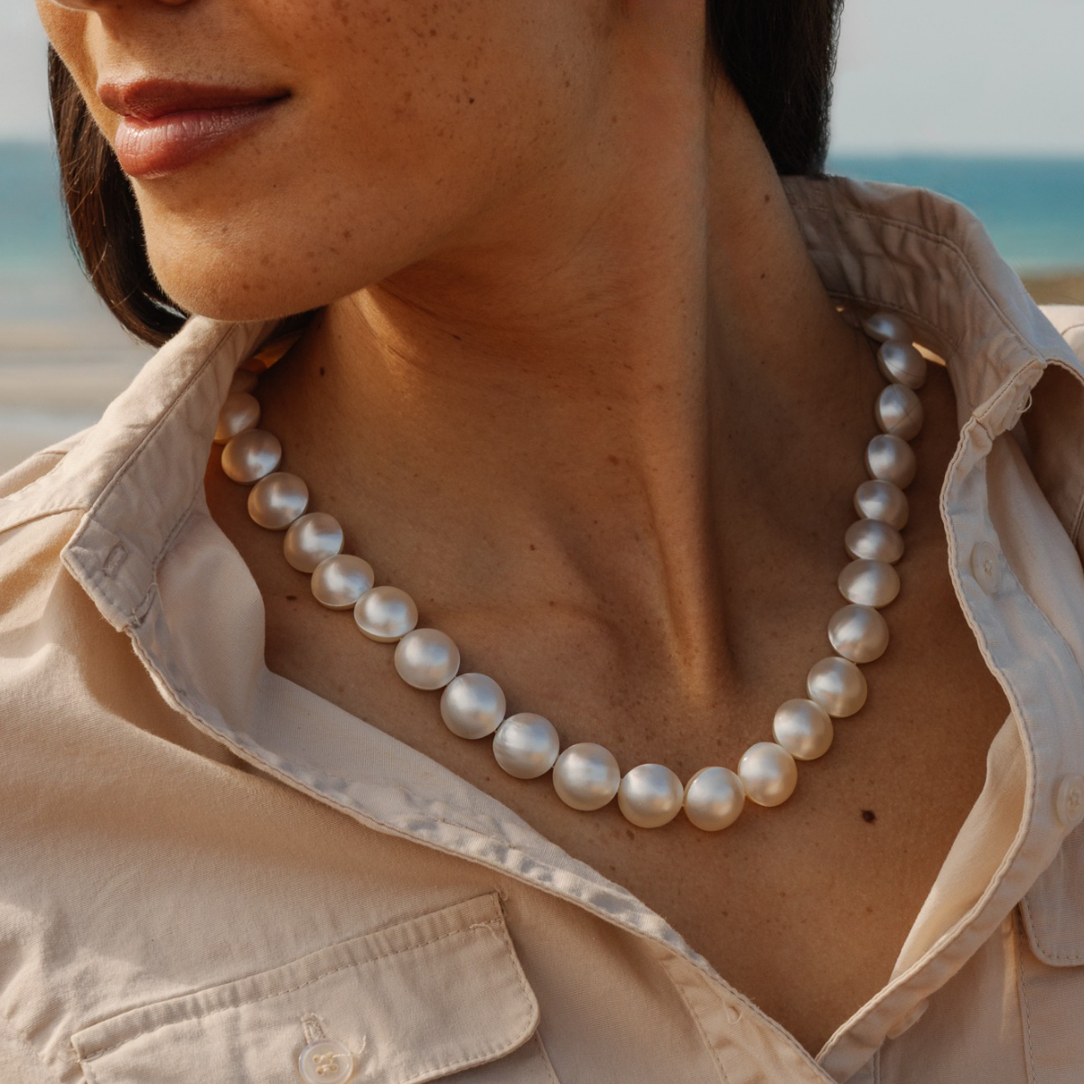 Person wearing a mabe pearl strand  necklace with a beach in the background