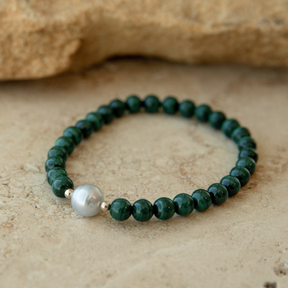 Green beaded malachite bracelet with a South Sea pearl on a beige stone background.