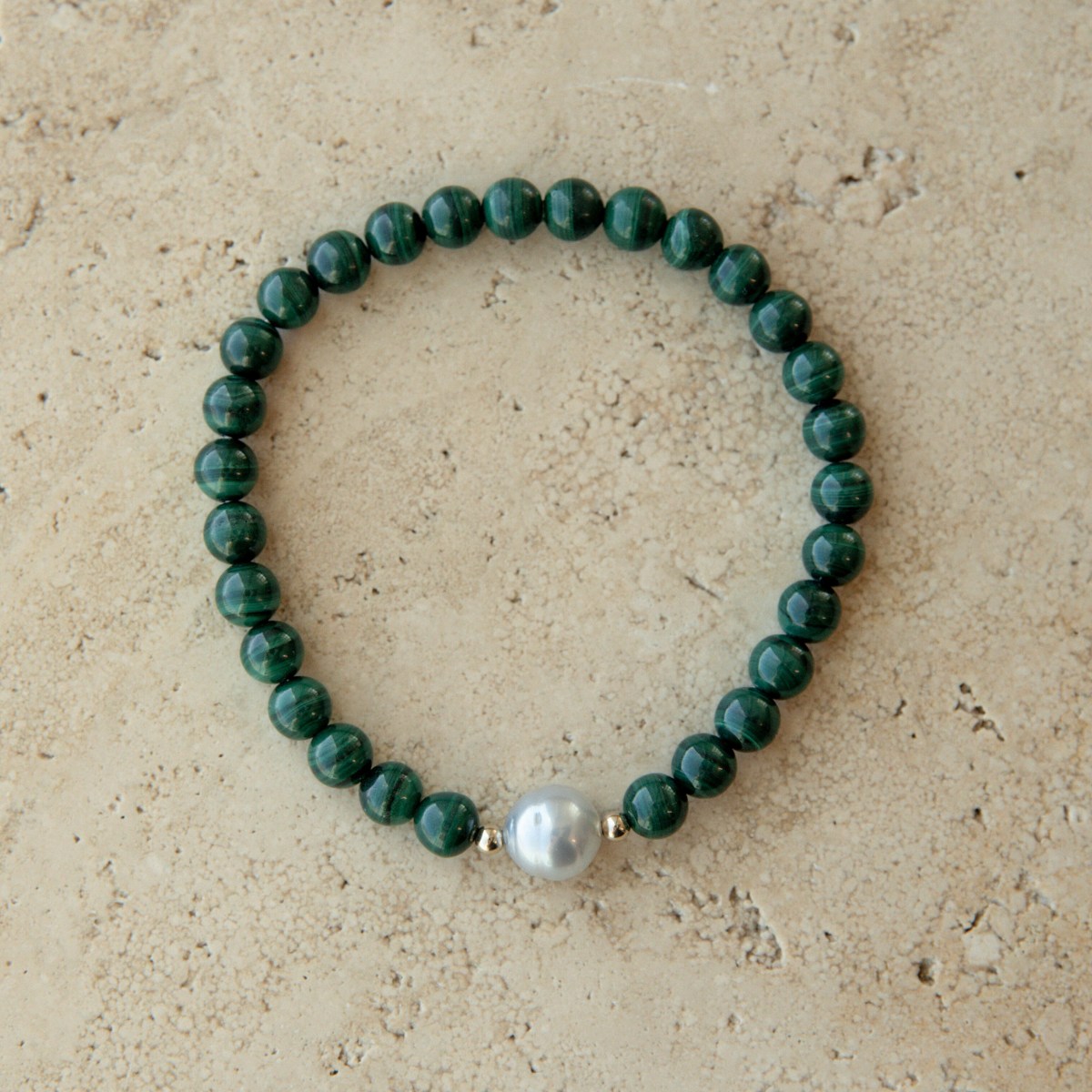 Green beaded malachite bracelet with a South Sea pearl on a beige stone background.