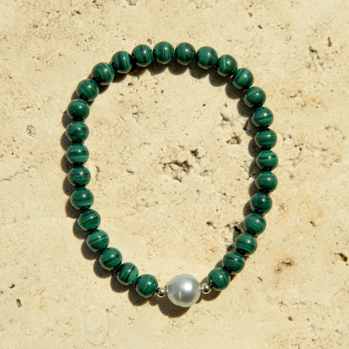 Green beaded malachite bracelet with a South Sea pearl on a beige stone background.