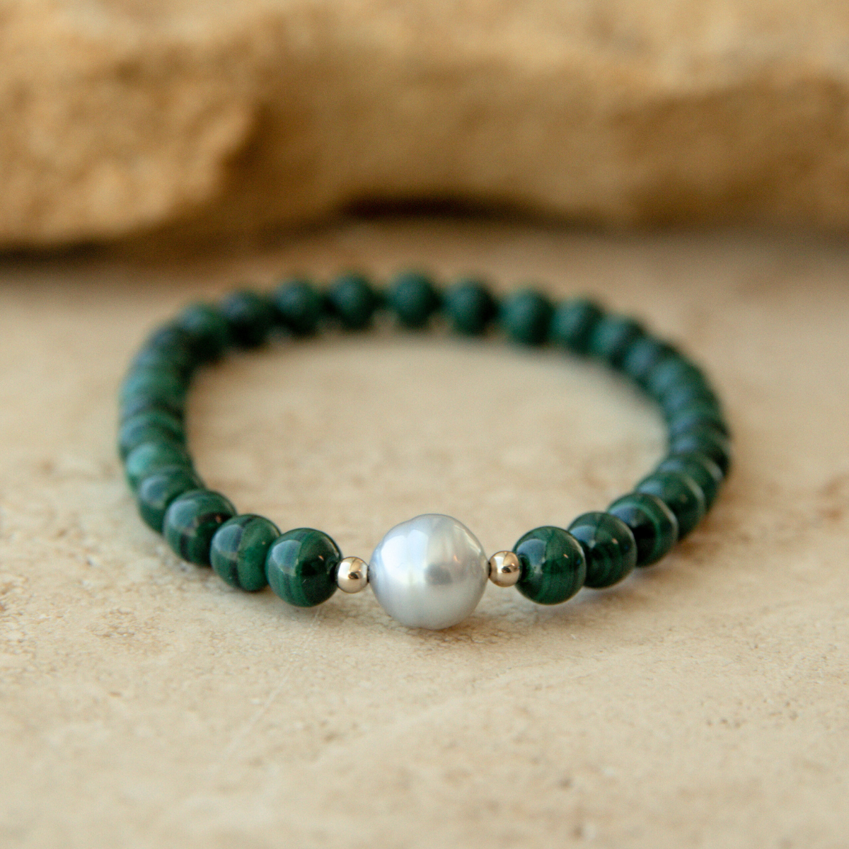 Green malachite beaded bracelet with an Australian South Sea circle pearl on a beige stone background