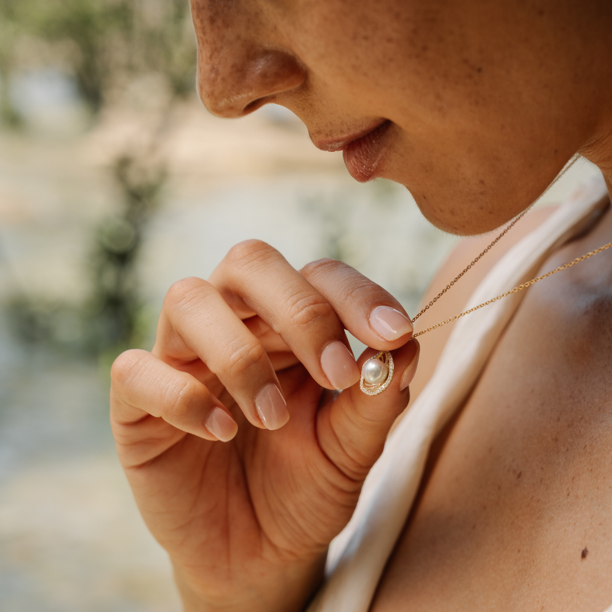 Person wearing a pearl necklace with a blurred natural background