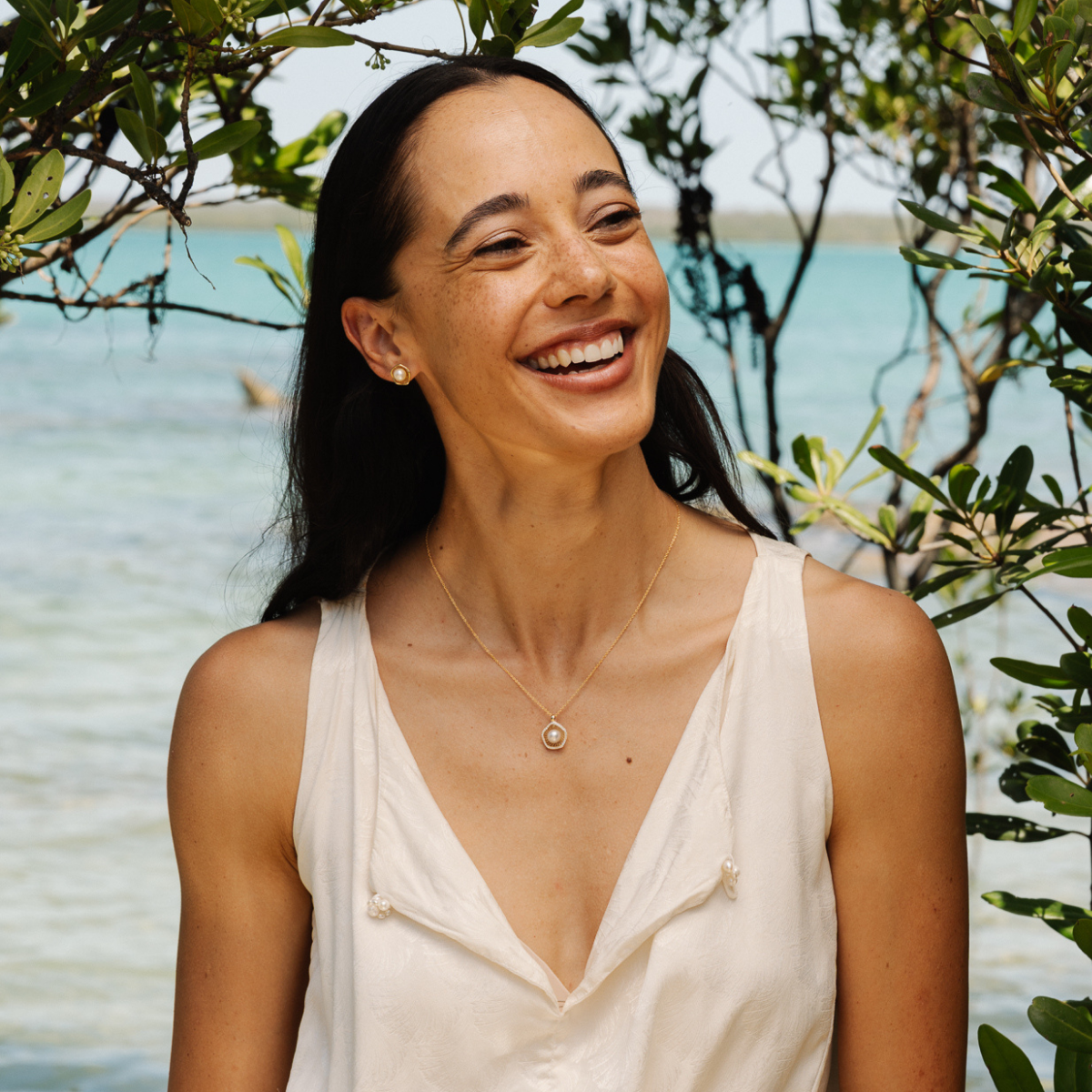 Woman smiling while standing under the Mangrove Trees at our pearl farm, wearing her Mangrove Lily pearl jewellery pieces.