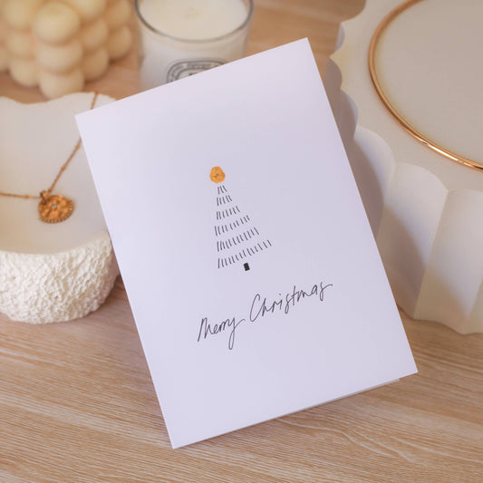 White card with Christmas tree design and 'Merry Christmas' text on a wooden surface.