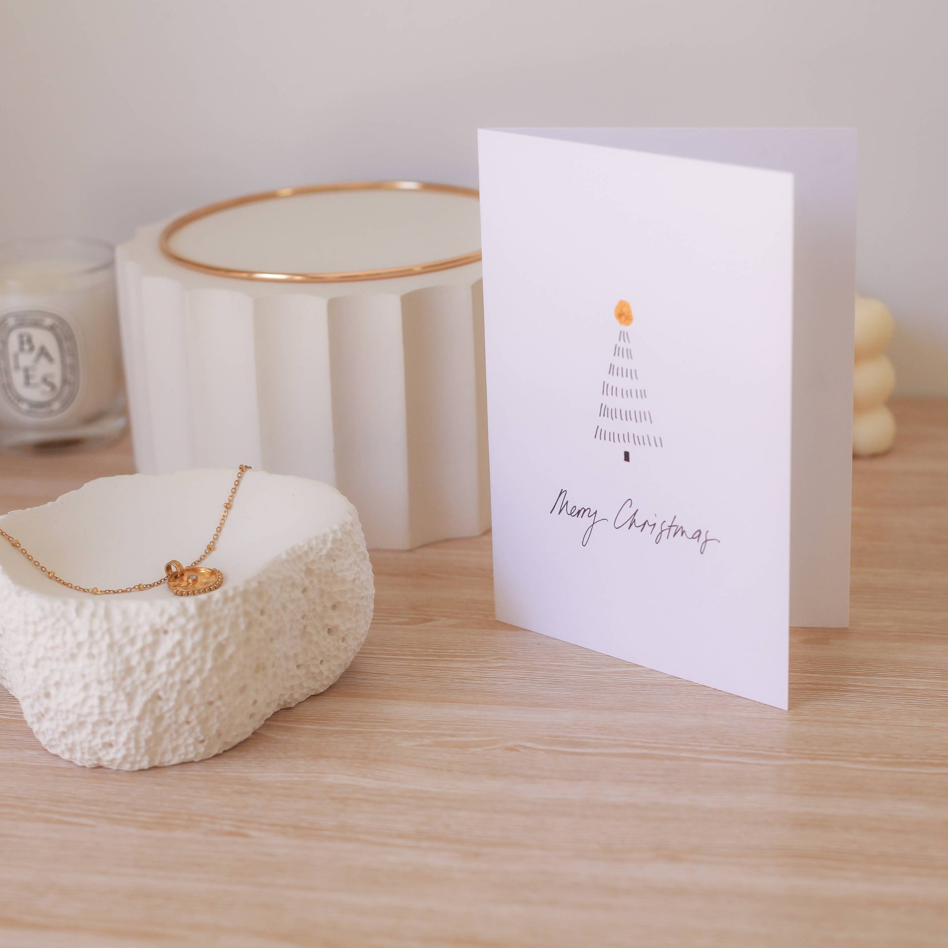 White candle, necklace, and Christmas card on a wooden surface