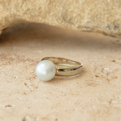 Gold ring with a pearl on a sandy background
