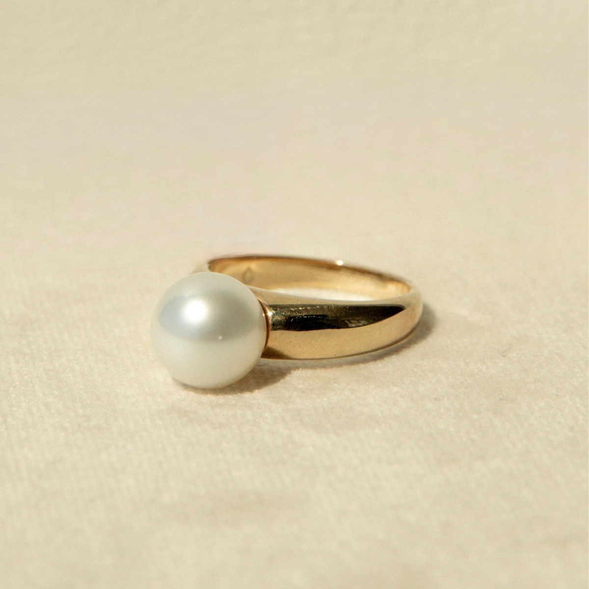 Gold ring with a pearl on a beige background