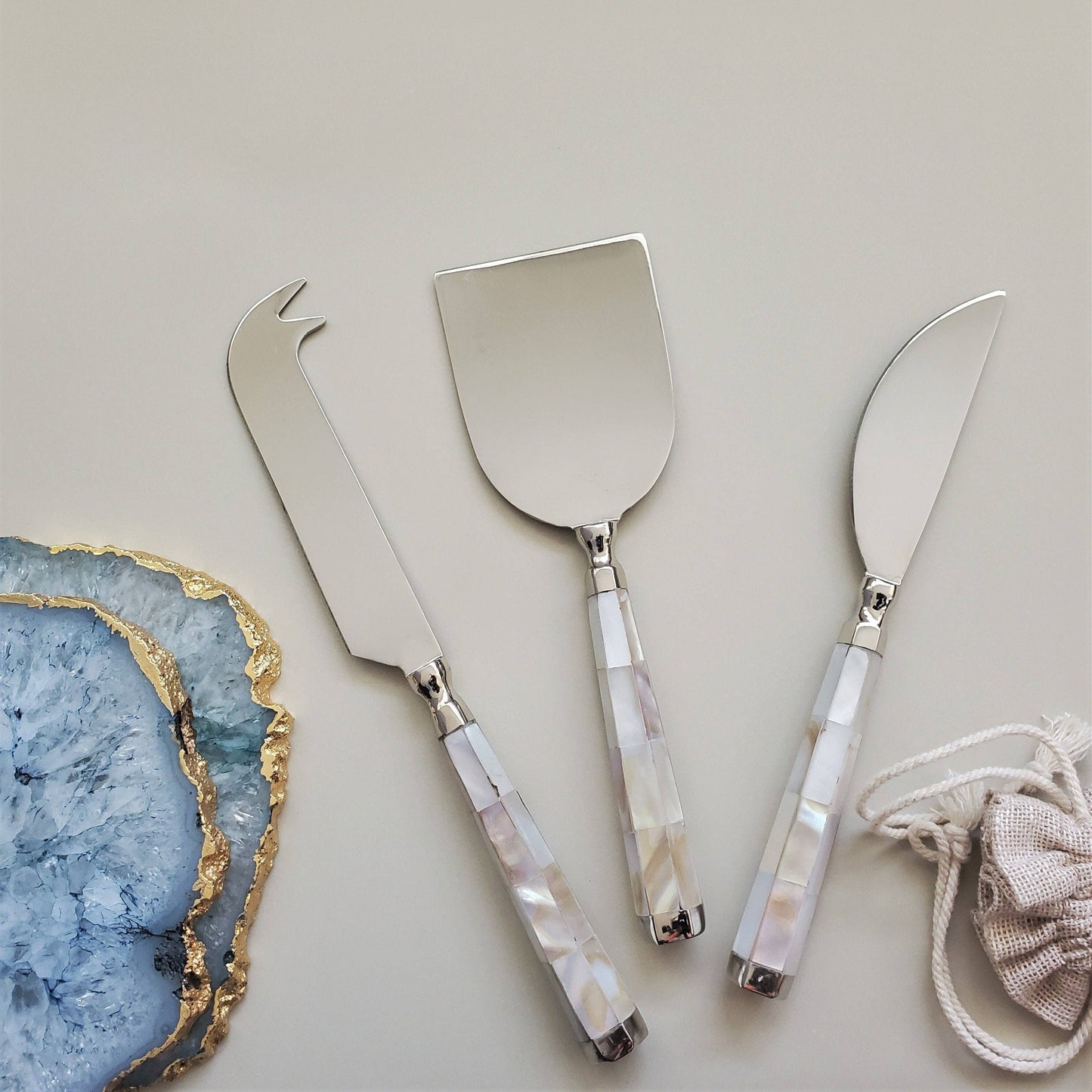 Set of three silver cheese knives with decorative handles on a light gray background