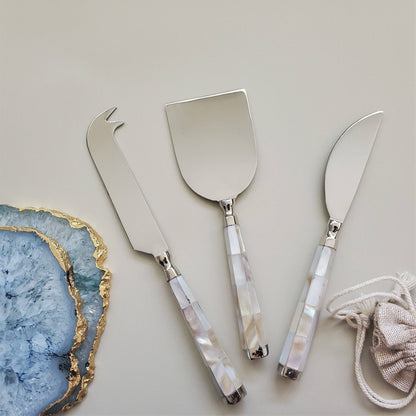 Set of three silver cheese knives with decorative handles on a light gray background