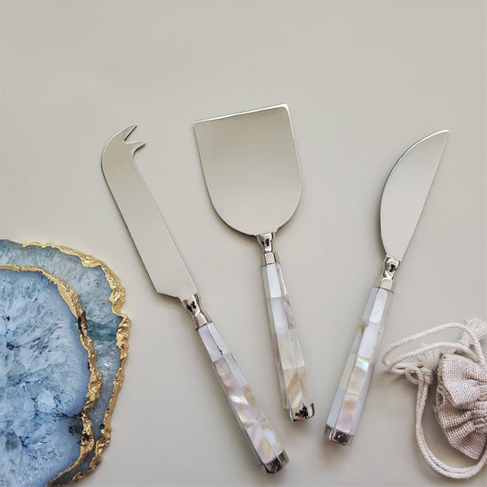 Set of three silver cheese knives with decorative handles on a light gray background