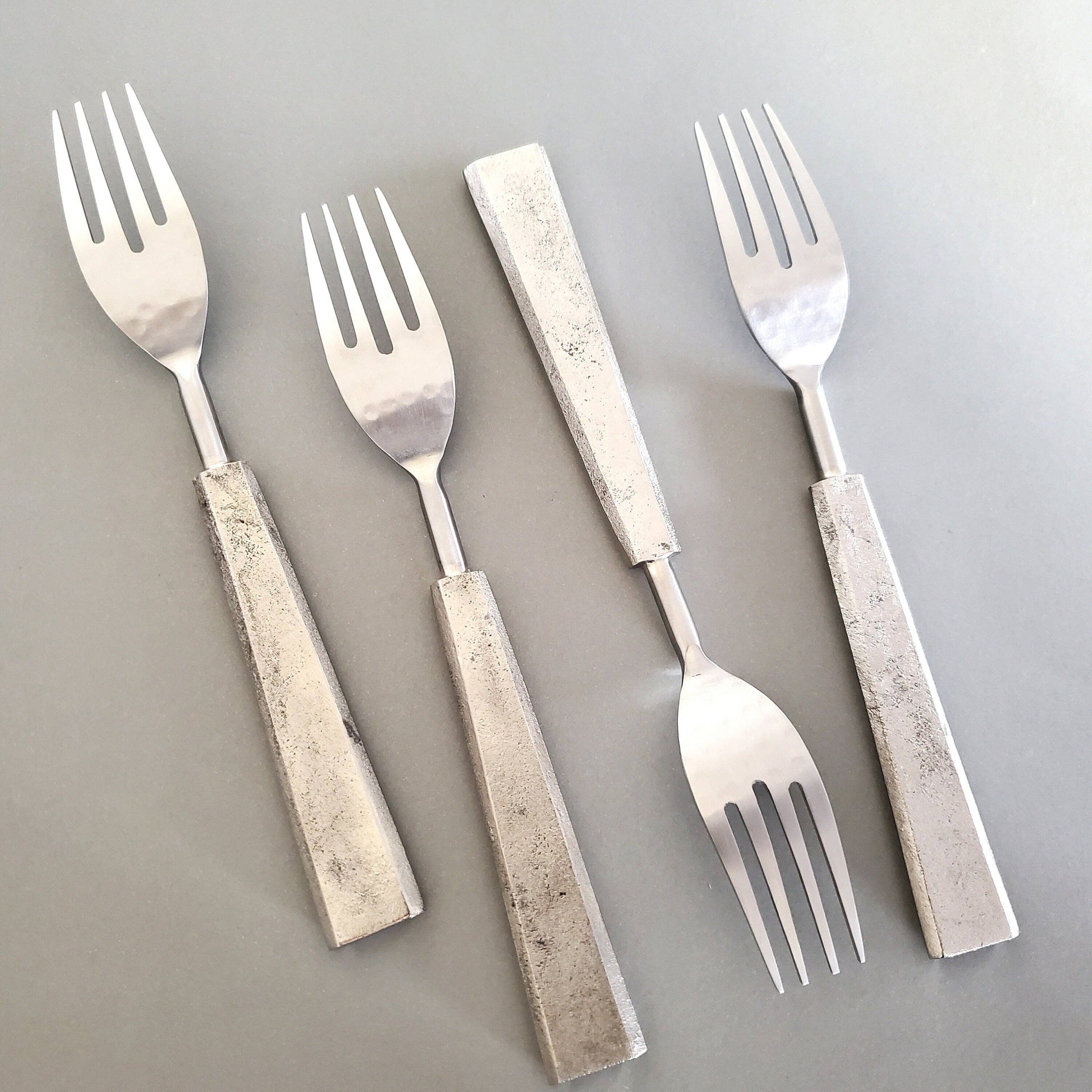 Four silver forks with textured handles on a gray background