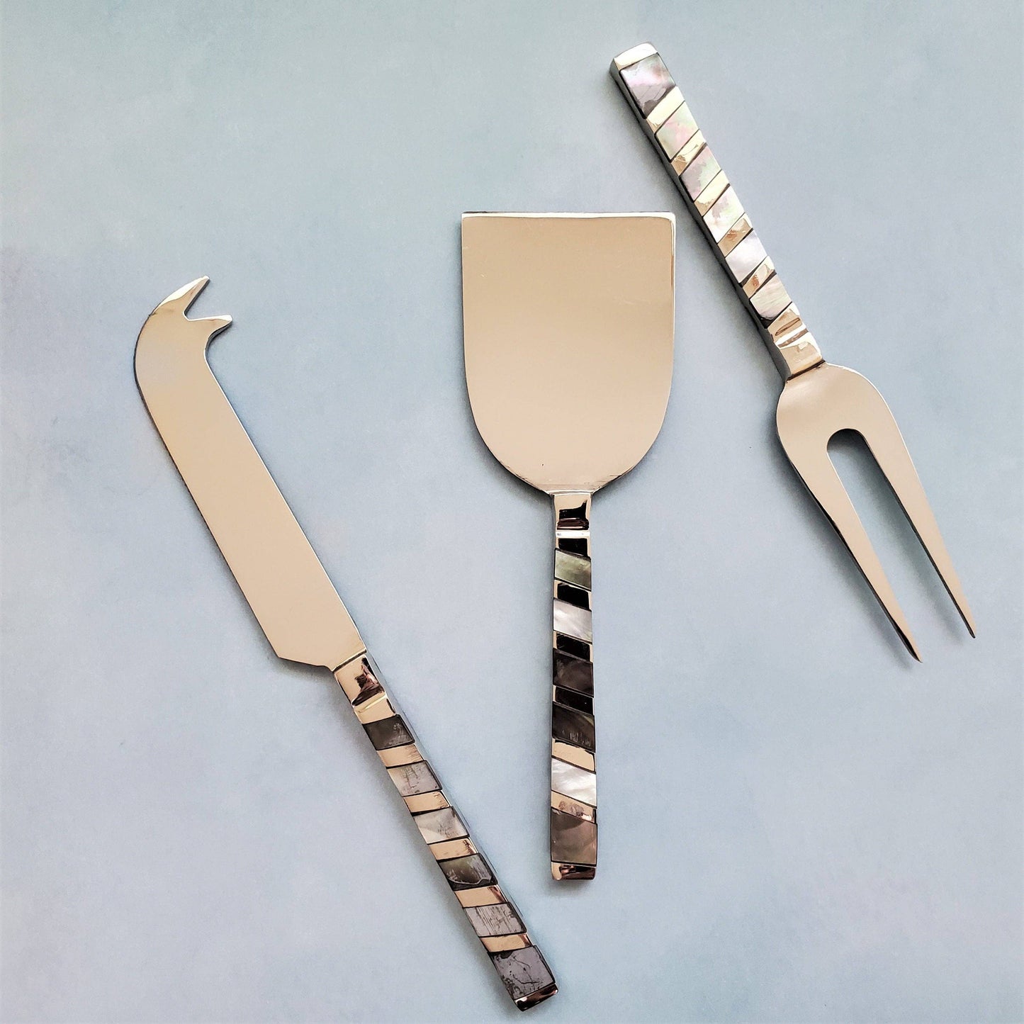 Set of three cheese tools with decorative handles on a light gray background