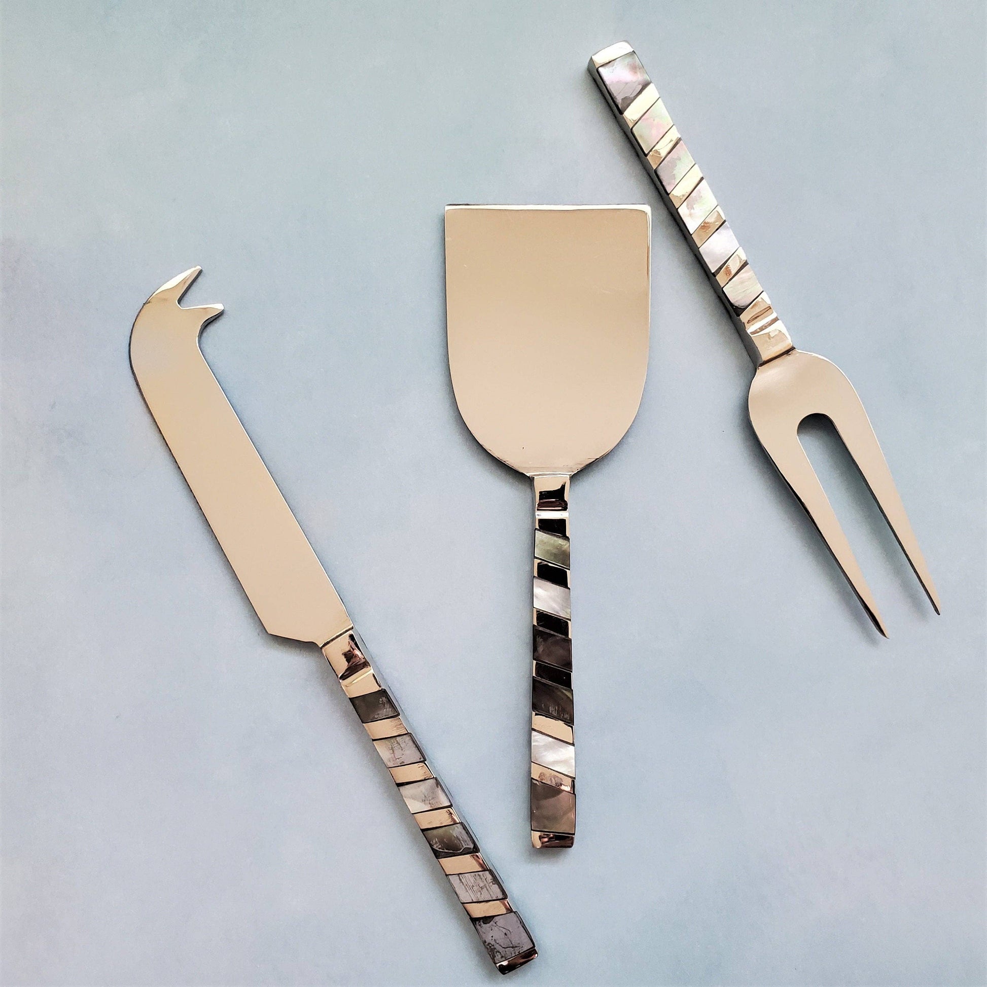 Set of three cheese tools with decorative handles on a light gray background