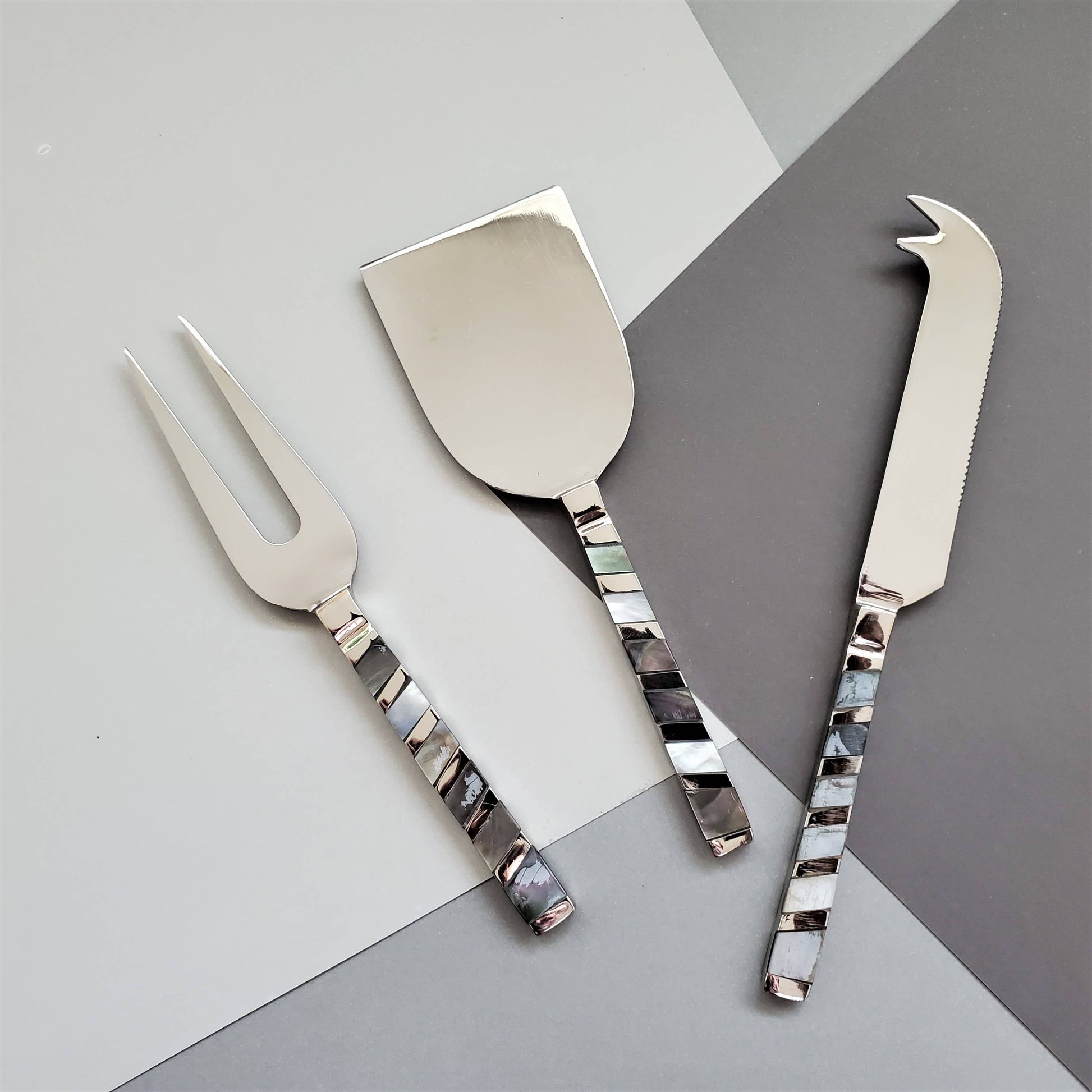 Set of three silver cheese tools with decorative mother of pearl handles on a grey background