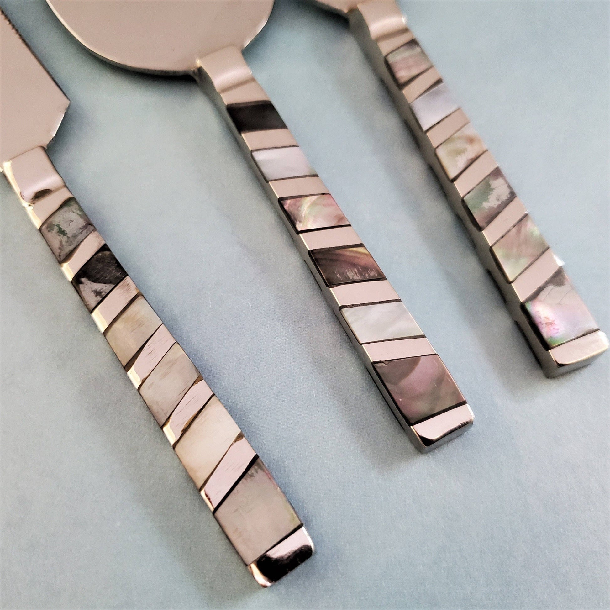 Set of silver cutlery with decorative mother of pearl handles on a light blue background