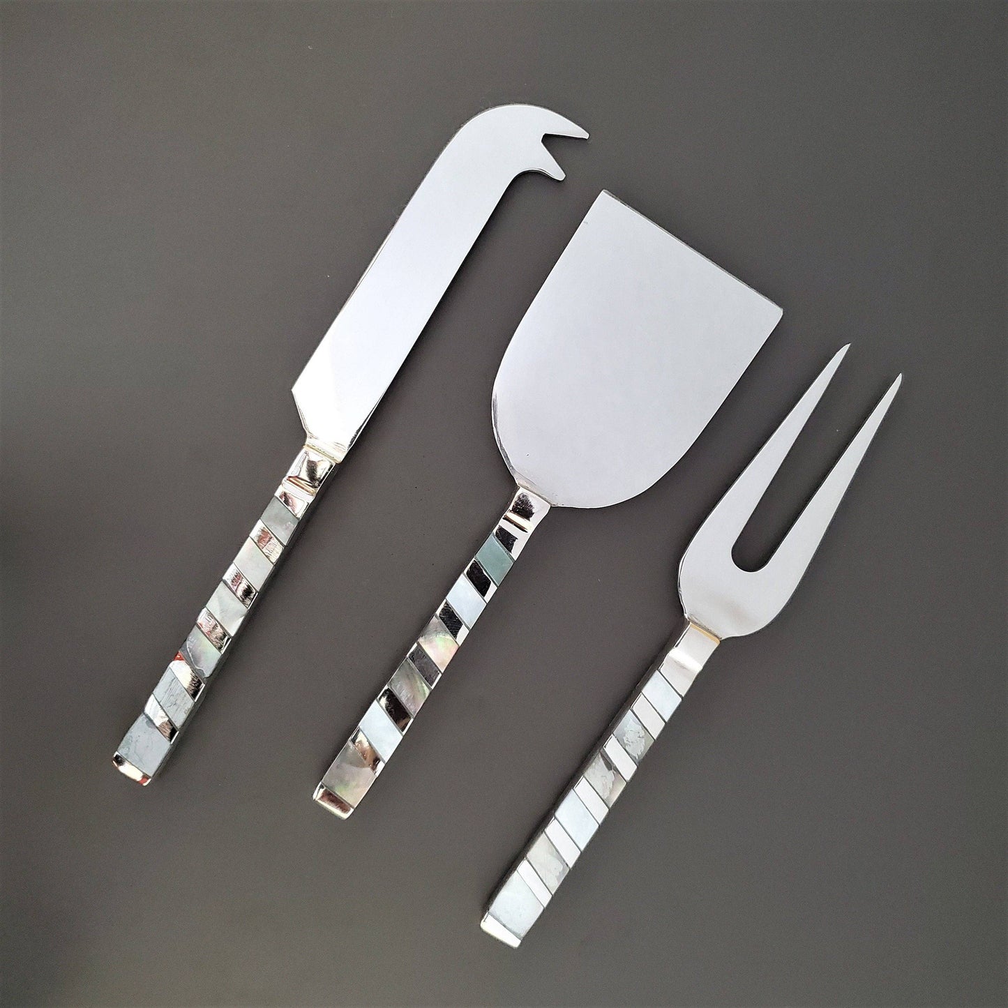 Set of three silver cheese knives on a dark gray background