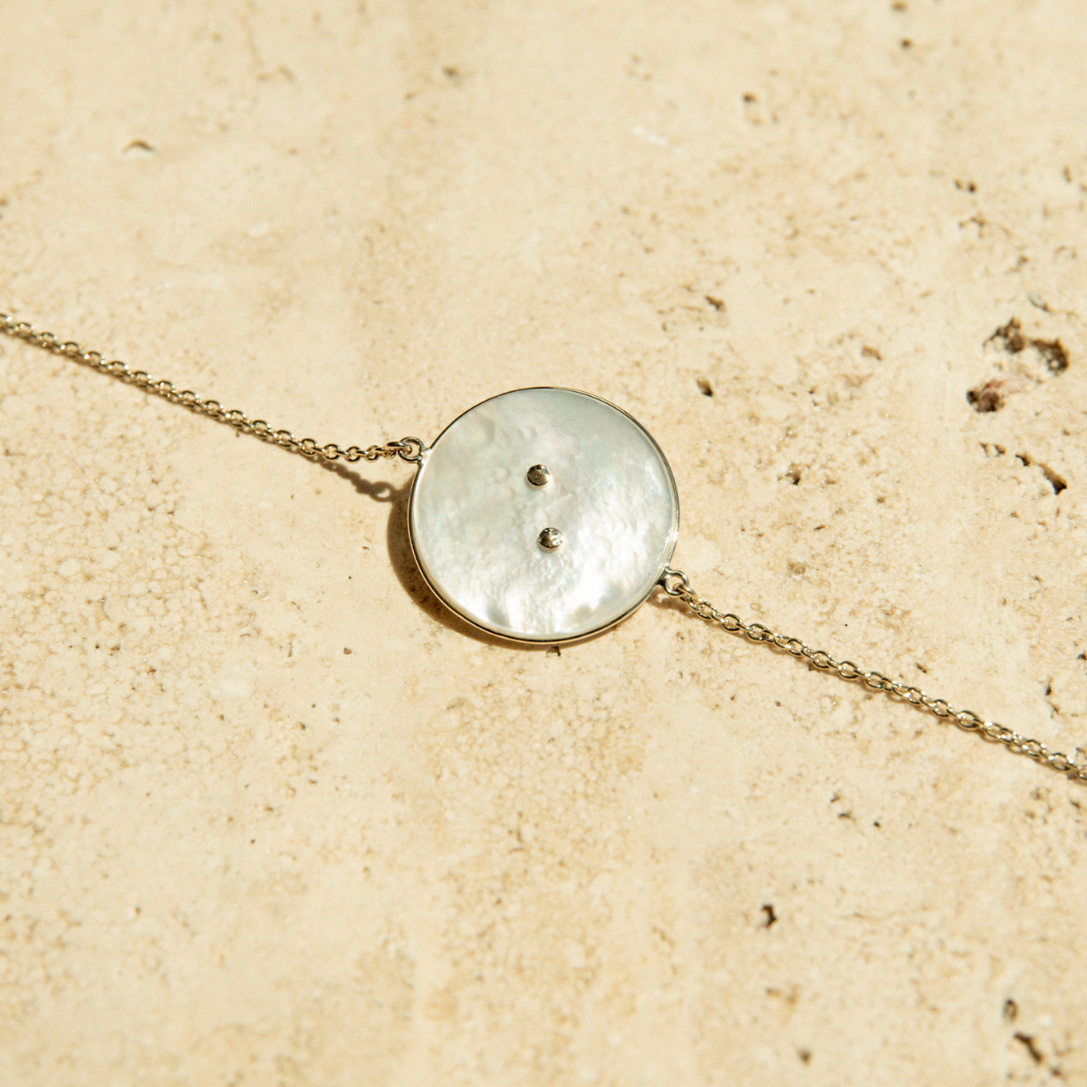 The back of the Mother of Pearl button charm on a chain bracelet.