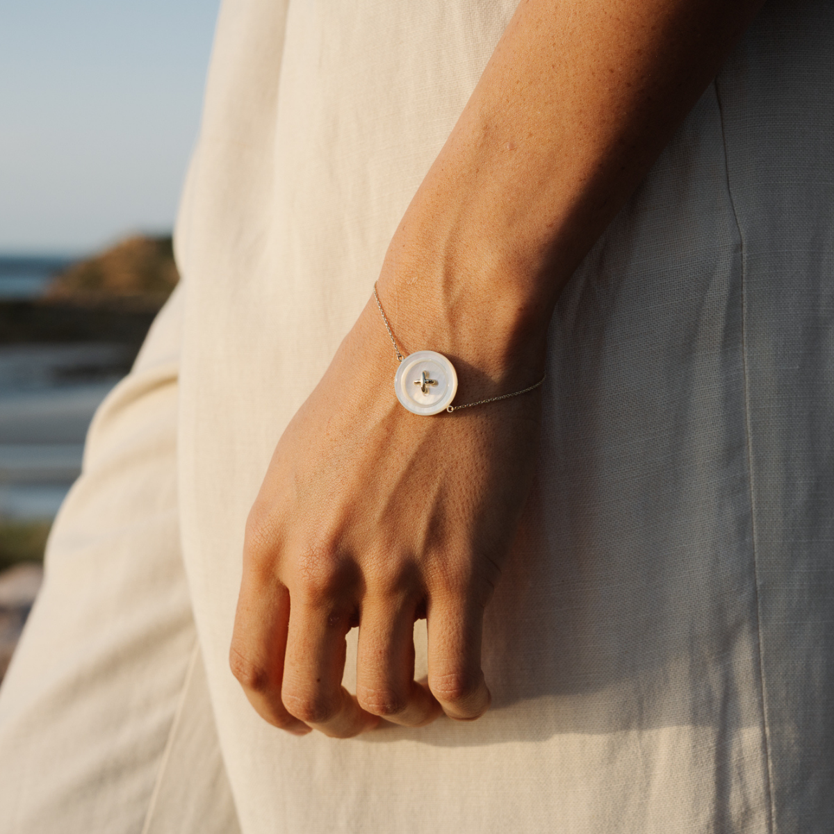 Person wearing a Mother of Pearl button chain bracelet on their wrist with a scenic background