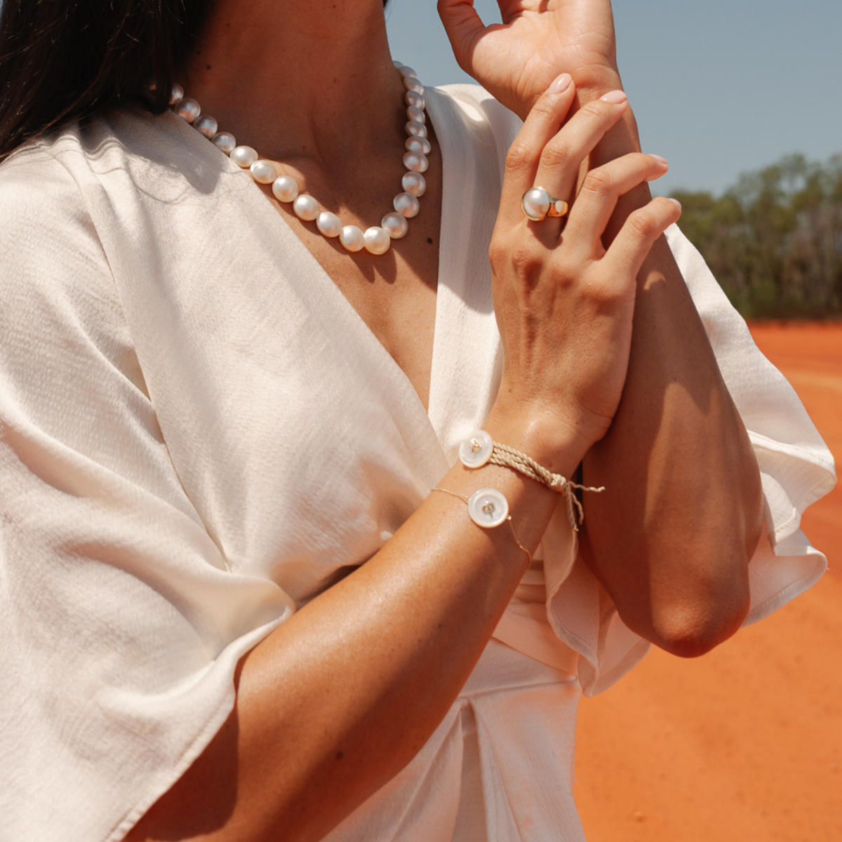 Close-up of a person wearing pearl jewellery with a blurred natural background