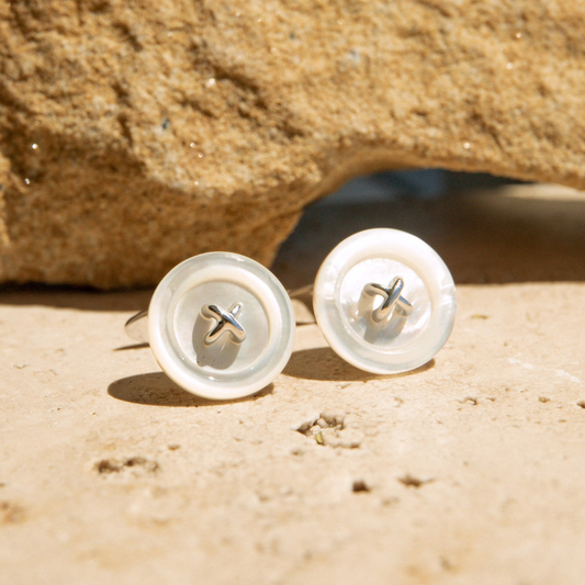 Pair of Mother of Pearl button earrings on a sandy surface with a rock in the background