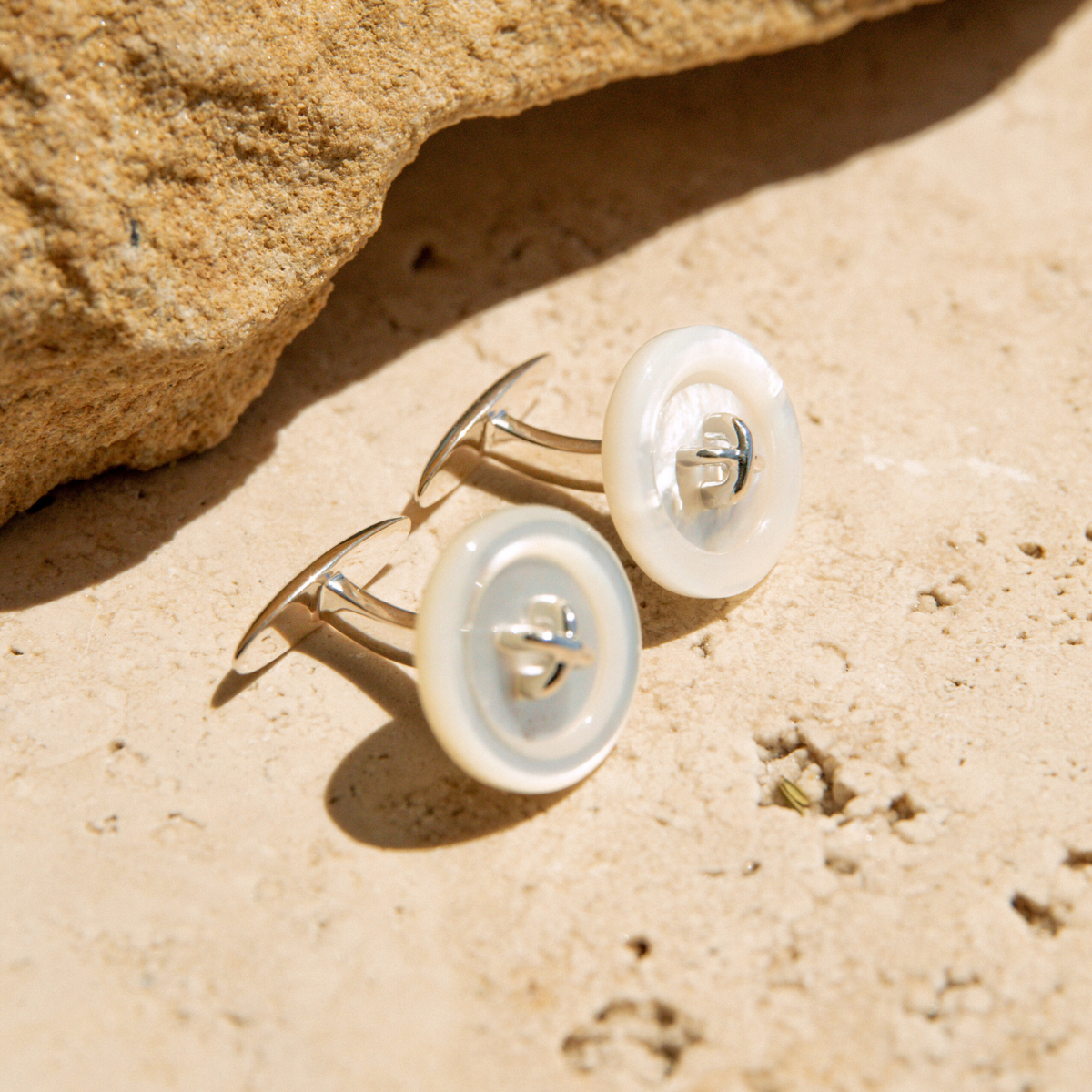 Mother of Pearl button earrings on a sandy surface with a rock in the background