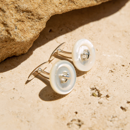 Mother of Pearl button earrings on a sandy surface with a rock in the background