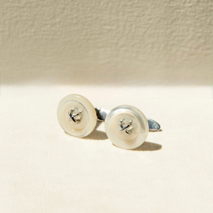 Pair of Mother of Pearl button earrings on a beige background