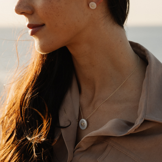 Close-up of a woman wearing mother of pearl button earrings and a matching mother of pearl button necklace with a blurred background.
