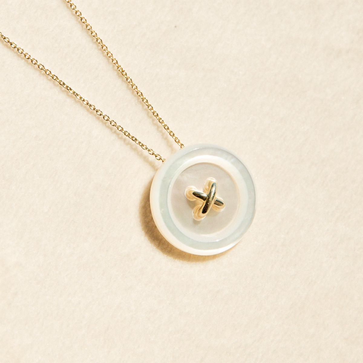 Necklace with a round Mother of Pearl button featuring a gold design on a beige background