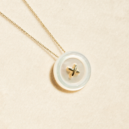 Necklace with a round Mother of Pearl button featuring a gold design on a beige background