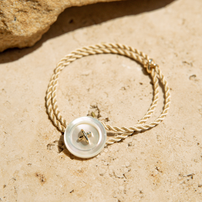 Bracelet with a Mother of Pearl button clasp and silk cord on a sandy surface