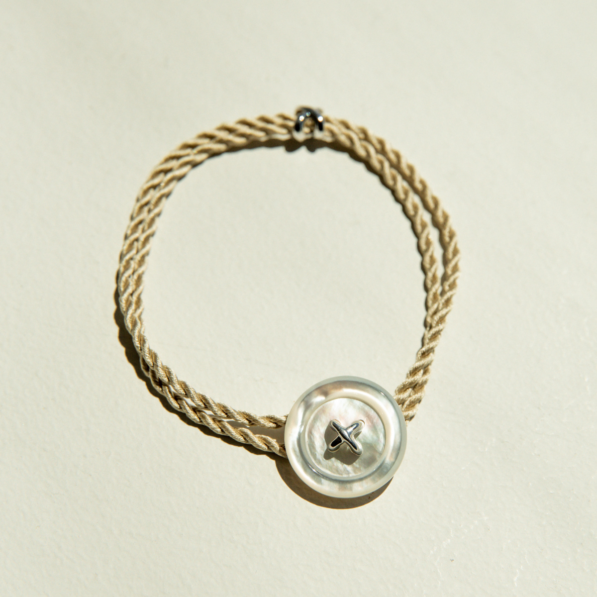 Mother of Pearl bracelet with a button clasp and silk cord on a beige background