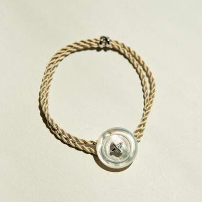 Mother of Pearl bracelet with a button clasp and silk cord on a beige background