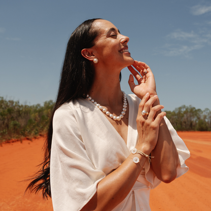 Woman in a white outfit with pearl jewellery standing in a desert landscape