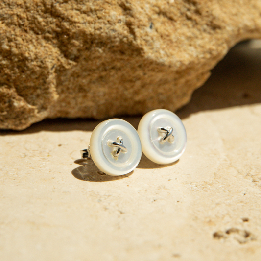Pair of Mother of Pearl earrings on a sandy surface with a rock in the background