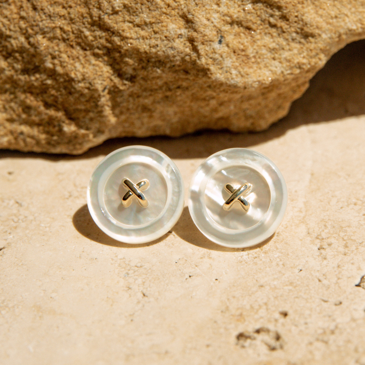 Pair of Mother of Pearl earrings with gold accents on a sandy surface