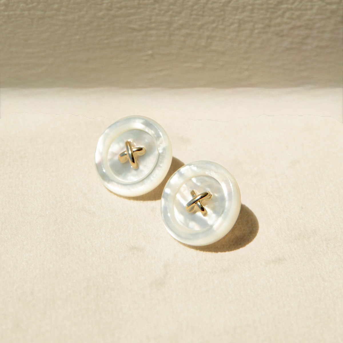 Mother of Pearl button earrings on a beige background