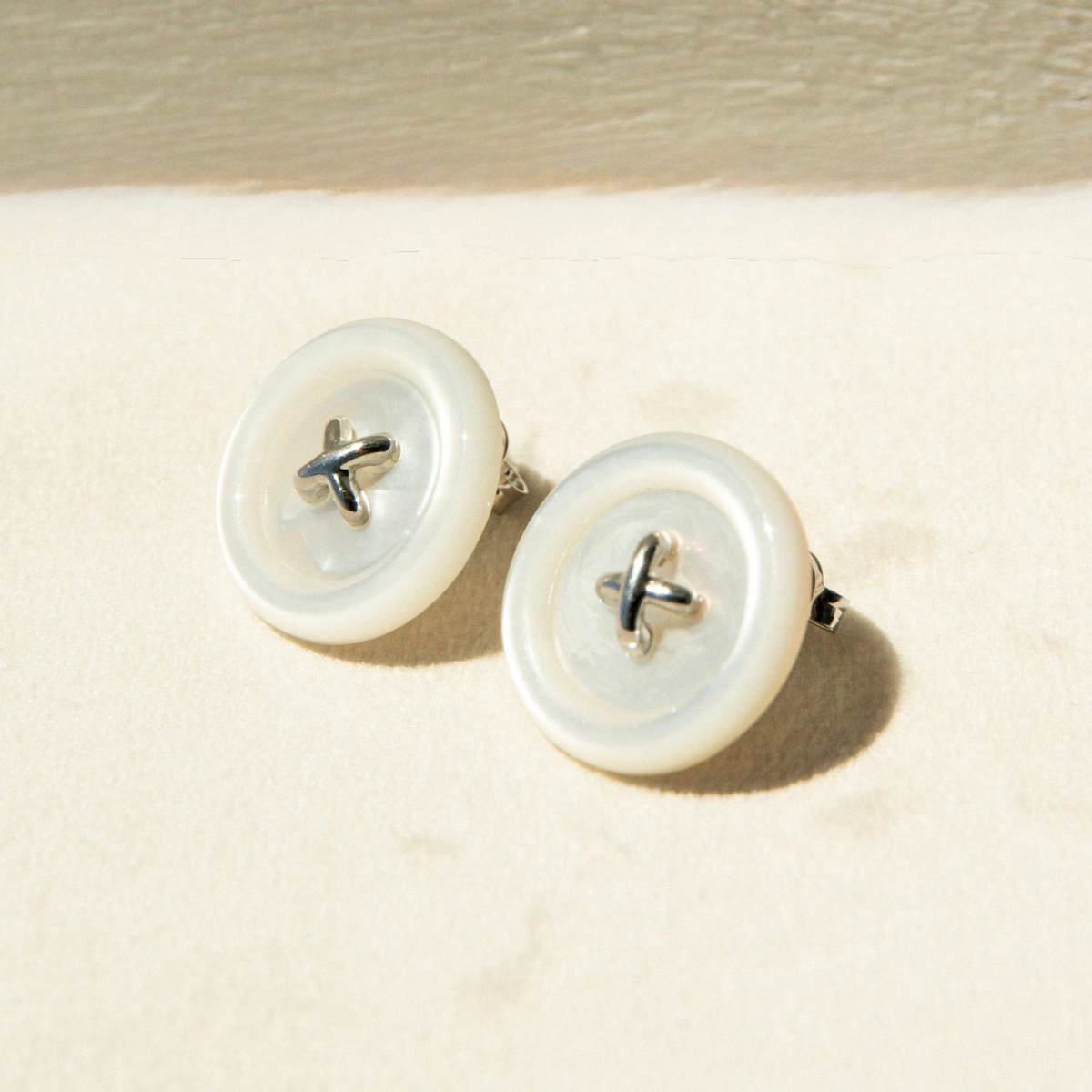 Pair of button Mother of Pearl earrings on a beige background
