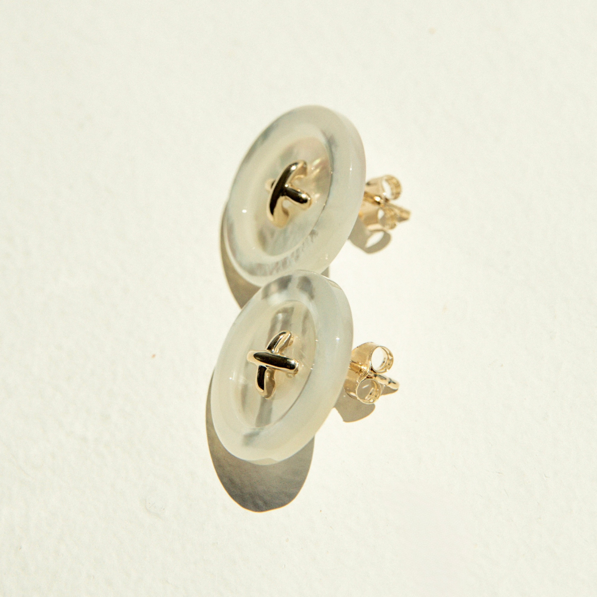 Pair of Mother of Pearl button earrings on a light beige background