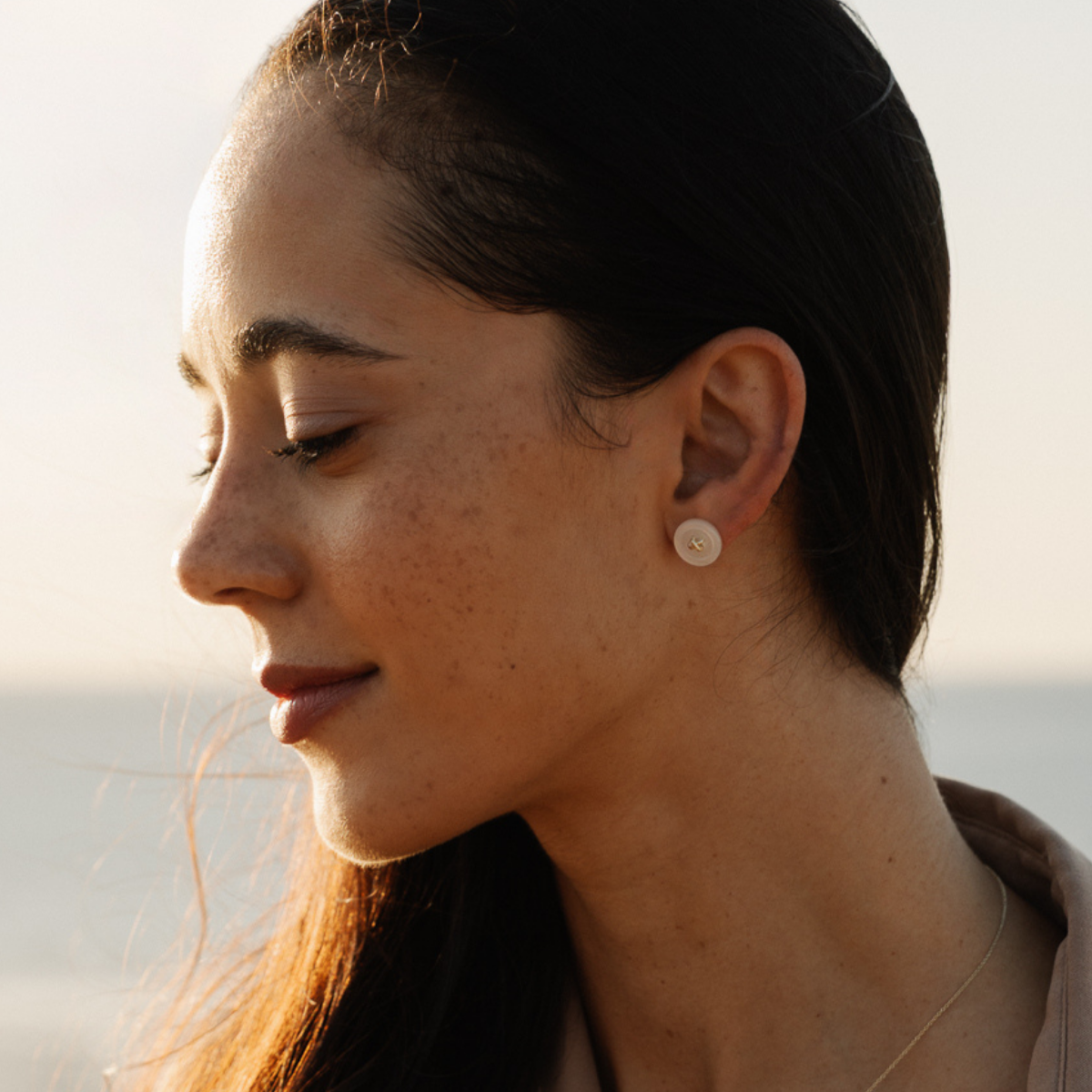 Close-up of a woman wearing a small Mother of Pearl stud earrings with a blurred background