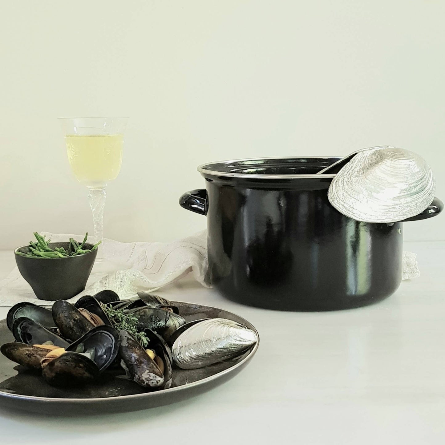 Black pot with mussels and mussel shovel on a white surface