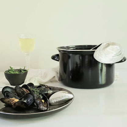 Black pot with mussels and mussel shovel on a white surface