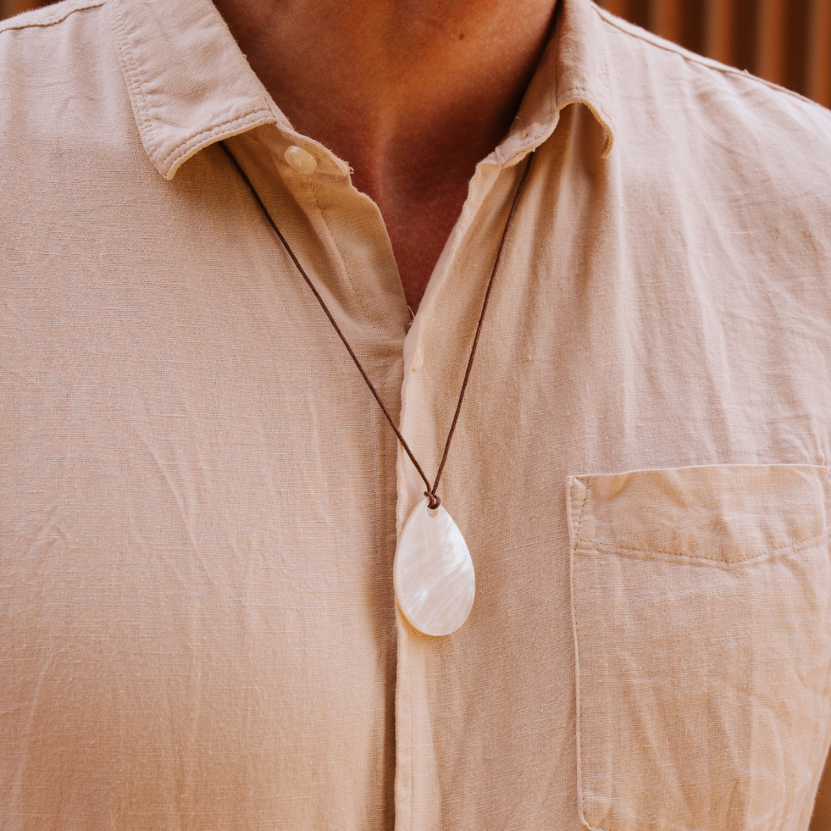 Person wearing a beige shirt with a necklace featuring a large white mother of pearl pendant.