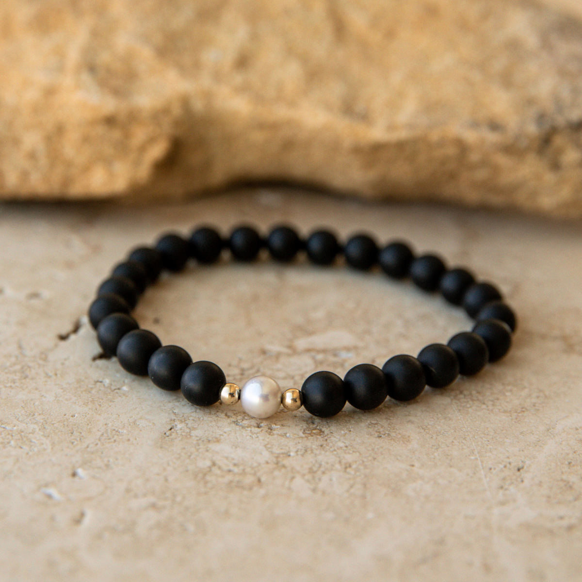 Black onyx beaded bracelet with a pearl and gold accent on a stone surface