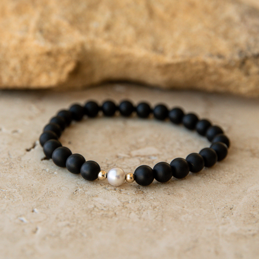 Black onyx beaded bracelet with a pearl and gold accent on a stone surface