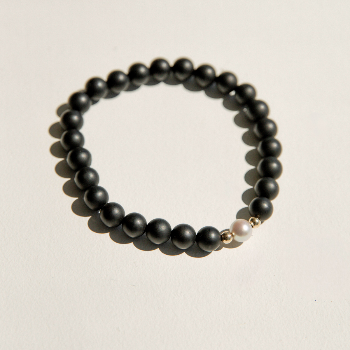 Black onyx beaded bracelet with a pearl charm on a beige background